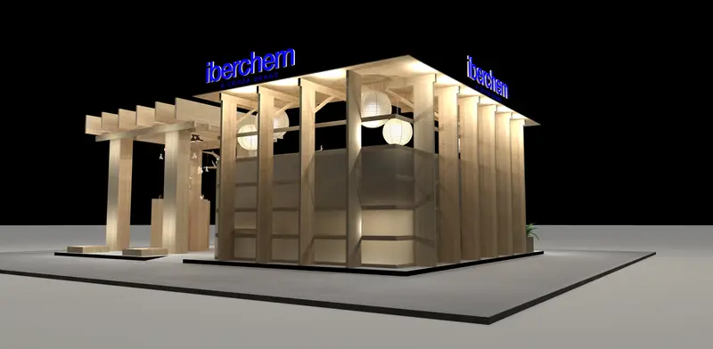 Vista cenital del mismo stand: pared de baldas, mesas altas de trabajo con taburetes, pérgola de vigas de madera y árbol escultórico sobre la barra curva